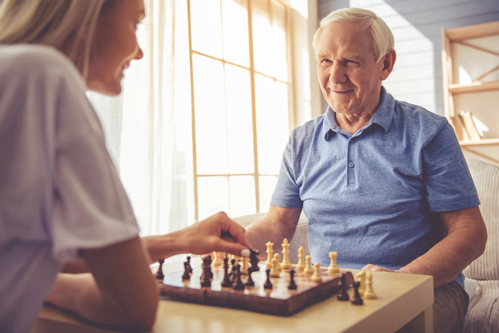 elderly man plays chess with younger lady